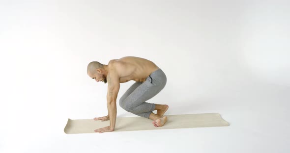 A Flexible and Plastic Male Yogi with a Beard Does Yoga on a Rug in a White Studio