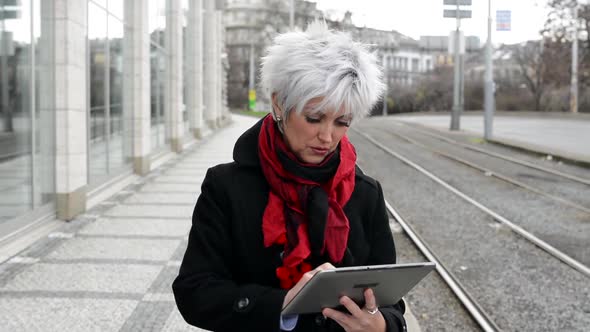 Middle Aged Woman Works on Tablet - Urban Street with Cars in the City