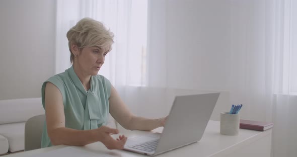 Aged Female Teacher Is Lecturing Online, Looking at Web Camera of Laptop, Distant Education By