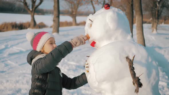 Girl Inserts a Nose on the Snowman