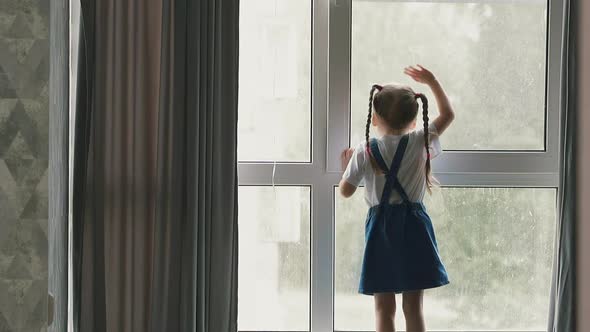 Girl in Denim Dress Waves Hand Looking Outside Large Window