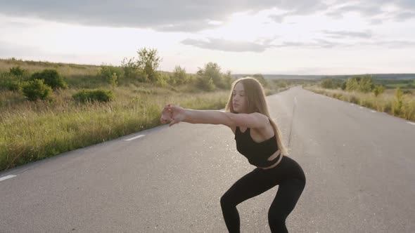 Pretty Athletic Girl Doing Squats and Warmup on the Road at Nature with Sunset