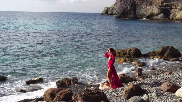 Side View a Young Beautiful Sensual Woman in a Red Long Dress Posing on a Rock High Above the Sea