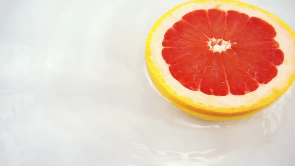 Rotating segments of ripe and juicy grapefruit in water on an white background. Slow motion.