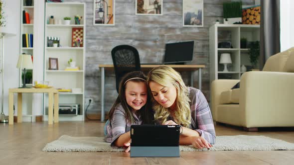 Cheerful Little Girl with Her Mother Lying on the Floor