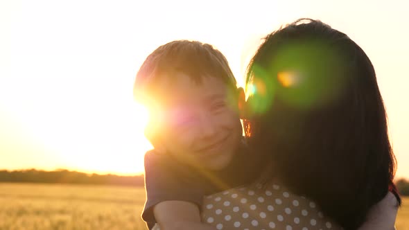 A Happy Little Boy Hugs His Mother. The Rays of the Sun at Sunset Illuminate His Face. The Concept