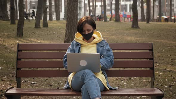 Woman working on laptop while sitting on bench in park. 