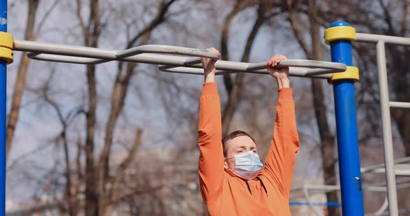 Man Pulls Up on the Bar Outdoor in a Surgical Mask