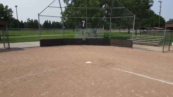 Pan out of empty ball field from home plate to second base. Foot prints in sand. Empty bleachers.