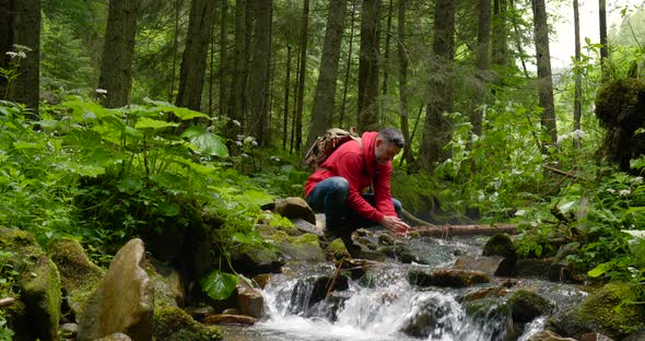 Bearded Man with a Backpack Washes His Hands with Water From a Mountain Stream
