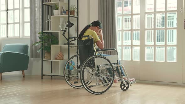 Disappointed Asian Kid Girl  Sitting In A Wheelchair Near Door In The House