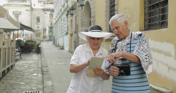 Senior Male and Female Tourists Standing with a Map in Hands Looking for Route