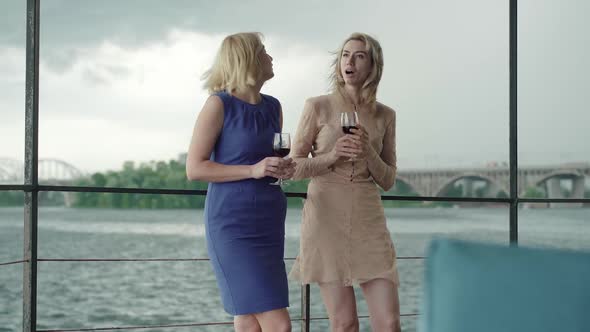 Wide Shot Portrait of Charming Women Talking and Holding Glasses with Red Wine. Confident Caucasian