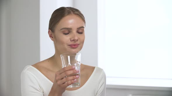 Woman Taking Pill, Drinking Water From Glass In White Interior