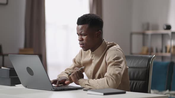 Sad Afroamerican Man is Using Laptop at Home Office Finding Mistake and Error of Program Grimacing
