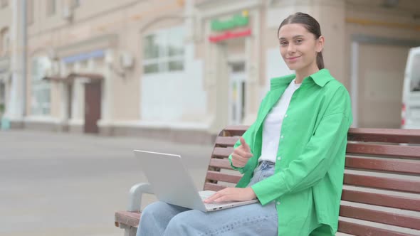 Hispanic Woman with Laptop Showing Thumbs Up Sign While Sitting Outdoor on Bench