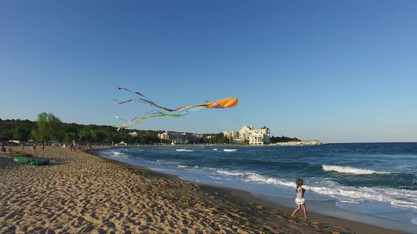 Little girl with flying kite on tropical beach at sunset. Child with beach toys.