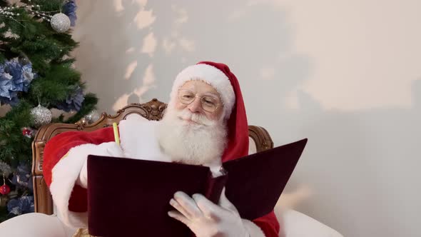 Santa Claus writing in a red cover book. Jotting down names or gifts for Christmas