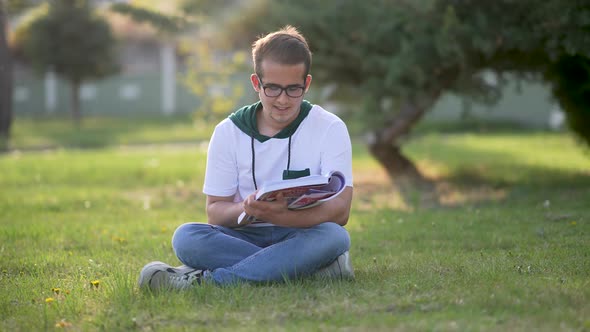 University student sitting on grass, writing essay, literary studies project