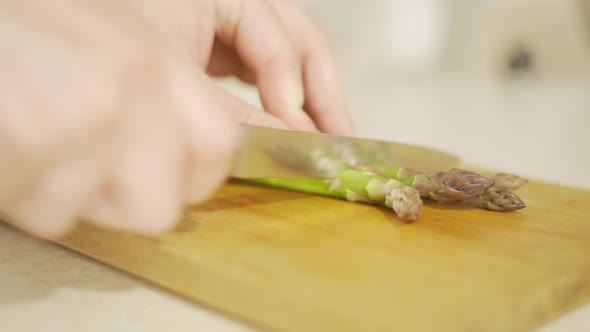 Hands Cut Green Asparagus with a Knife on a Wooden Board Closeup