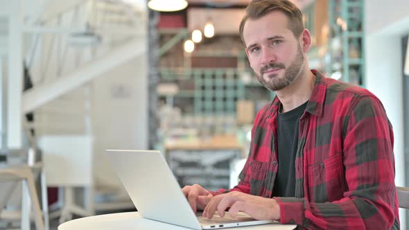 Thumbs Up By Positive Young Man with Laptop in Cafe