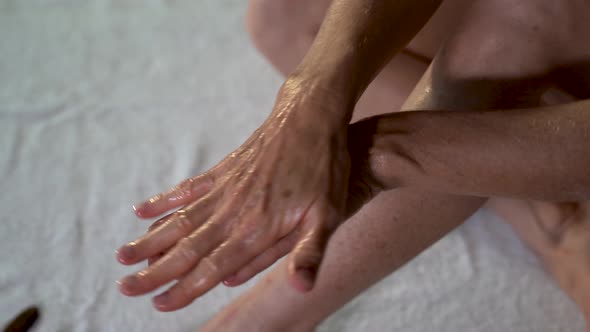 Closeup of mature woman rubbing coconut oil on her hands preparing for leg massage.