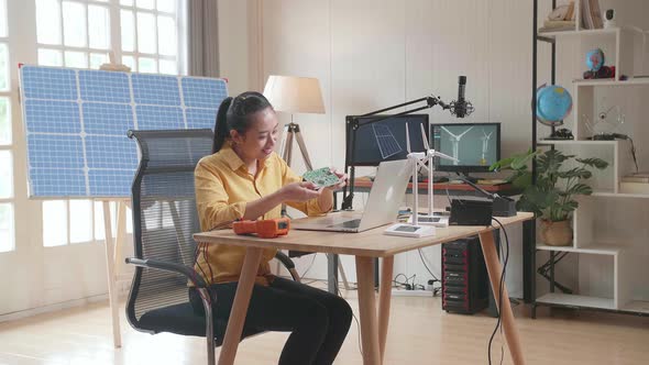 Asian Woman With Wind Turbine Looking At Circuit Board While Working With Laptop