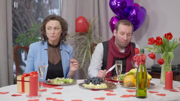 Angry Caucasian Man Standing Up From Valentine's Dinner Table and Leaving Woman Alone Passing Camera