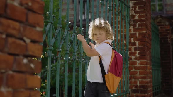 Little Schoolboy Standing Near Gate Playing Looking at Camera and Smilling Outside Near School