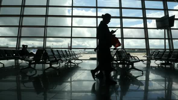 Travelers Walking Along Window in Airport Terminal, People Silhouettes Walking.