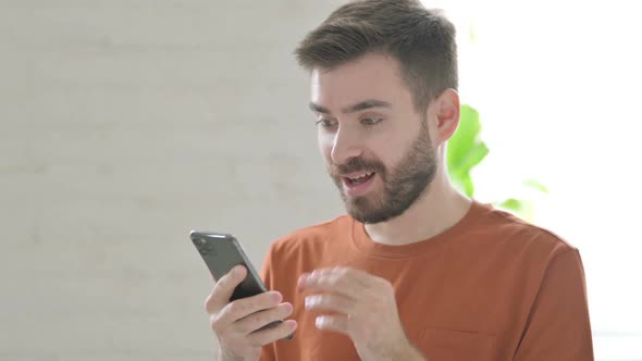 Young Man Celebrating Success on Smartphone