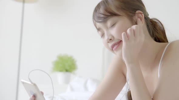 Young asian woman lying happy earphone listening music with relax and enjoy in the bedroom.