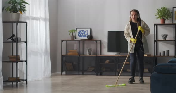 Positive Teen Girl Is Washing Floor in Apartment Listening To Music By Headphones and Player Doing