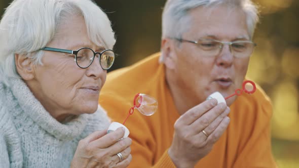 Romance at Old Age. Elderly Couple Blowing Soap Bubbles in the Park in Autumn