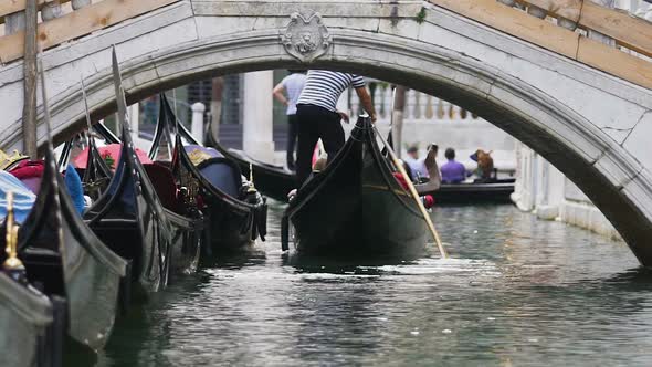 Several gondolas carrying tourists along narrow channel with bridge, boats aside