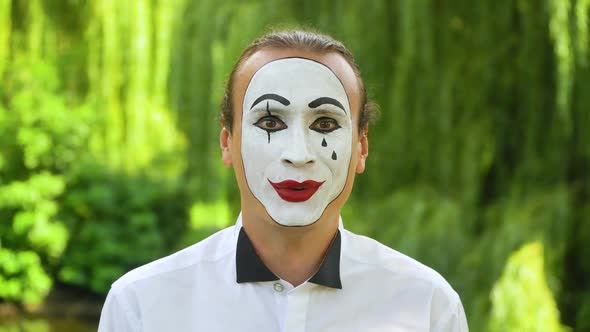 Close-up of a Mime Looking at the Camera and Smiling on Green Background in a Park. Emotion of Joy