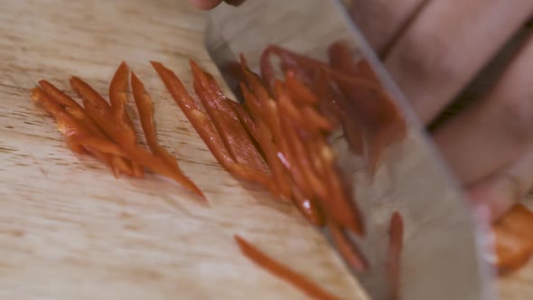 Cutting a Spicy Red Chilli into thin Slices on a wooden Cutting Board - Close Up