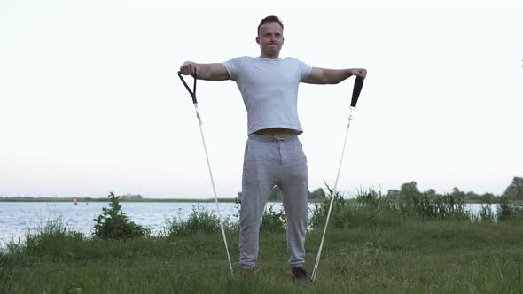 The athlete performs exercises with the help of an expander on the street in quarantine.