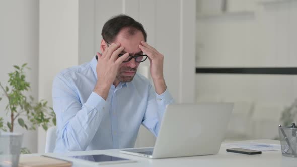 Middle Aged Man with Headache Working on Laptop in Office
