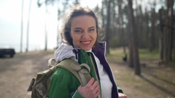 Joyful Woman with Backpack Smiling Looking at Camera Standing in Sunlight in Spring Autumn Forest
