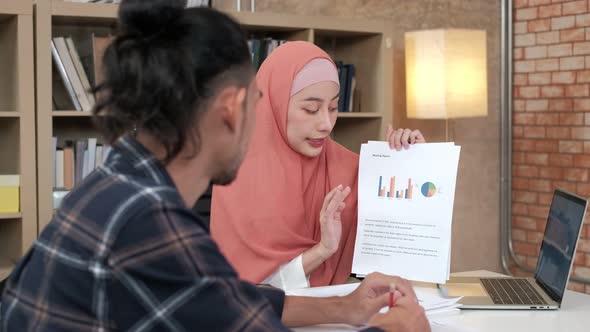 Two young Islamic colleagues work in a small startup office.