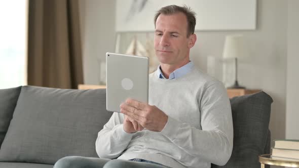 Cheerful Middle Aged Businessman Using Tablet on Sofa