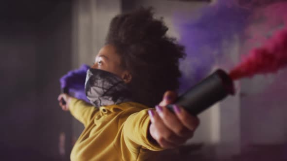 Mixed race woman holding blue and purple flares standing in an empty building