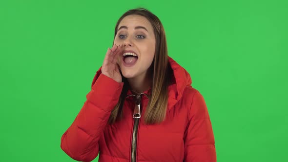 Portrait of Lovely Girl in a Red Down Jacket Is Screaming Calling Someone. Green Screen
