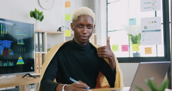 guy with blue eyes and white hair sitting near digital computer smiling looking at camera