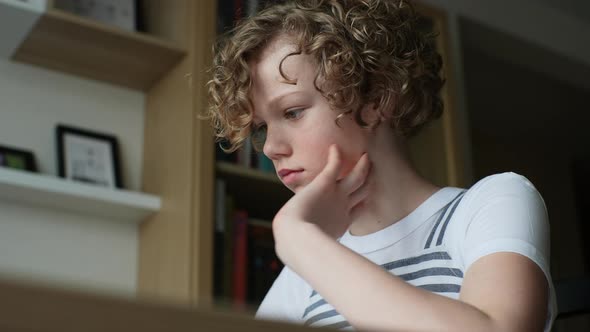 Closeup Lowangle View of Tired Child Schoolgirl Writing Homework Holding Head with Hand Sitting at