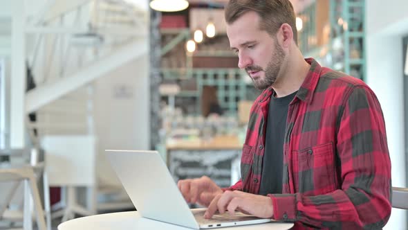 Coughing Young Man Using Laptop in Cafe