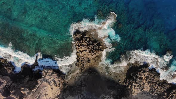 Top-down view over ocean waves crashing on rocky coast near Porto dos Frades, Madeira.