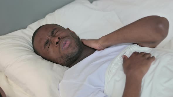 Exhausted Young African Man with Neck Pain in Bed