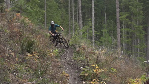 A young man mountain biking in a forest on a mountain.